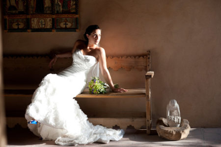Bride in white dress on Southwestern bench with adobe wall