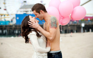 Couple kissing with pink balloons in front of pier