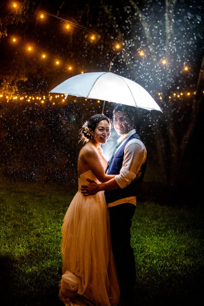 Bride and Groom in the night rain with umbrella and string lights