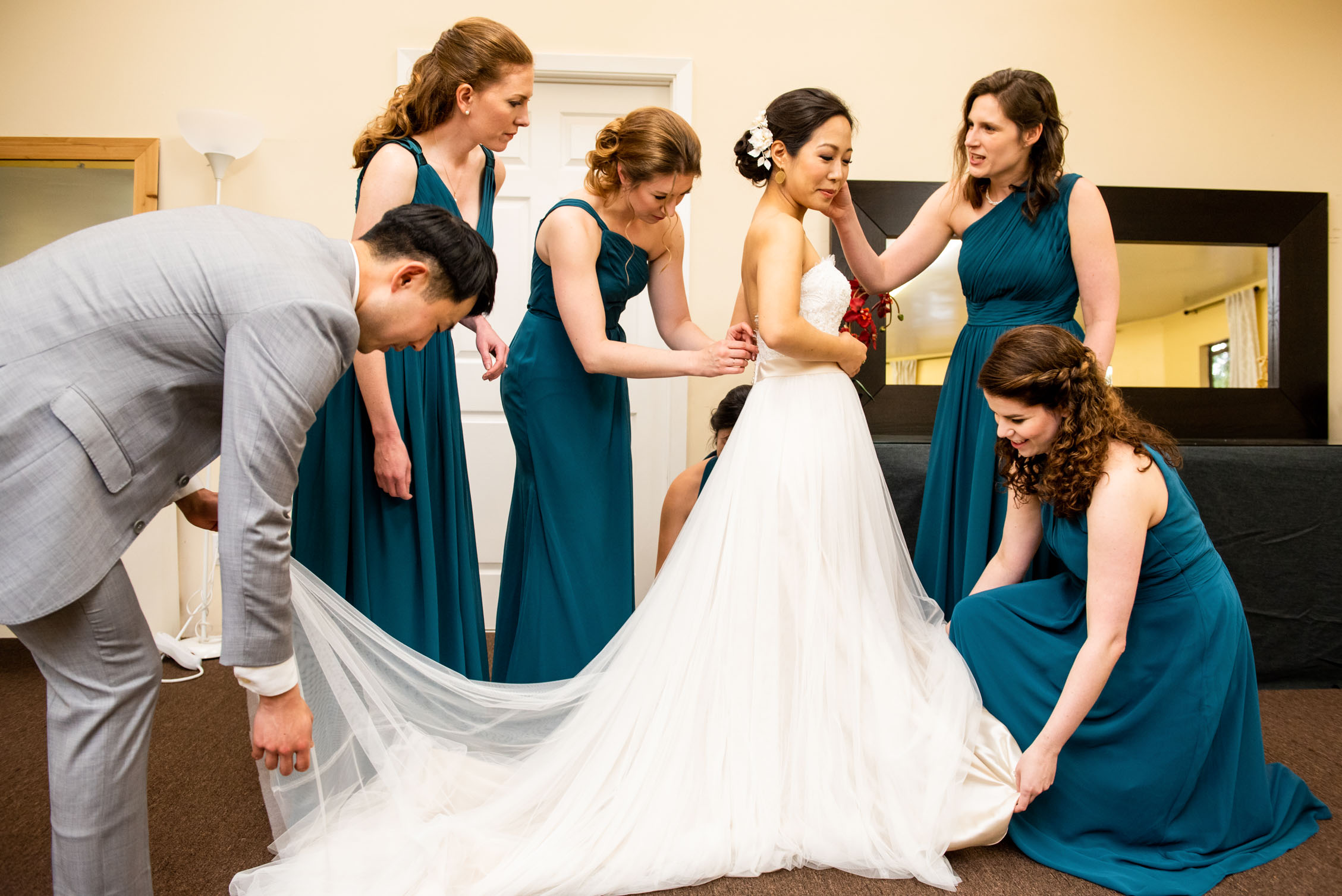 Four bridesmaids and bridesman help the bride get ready