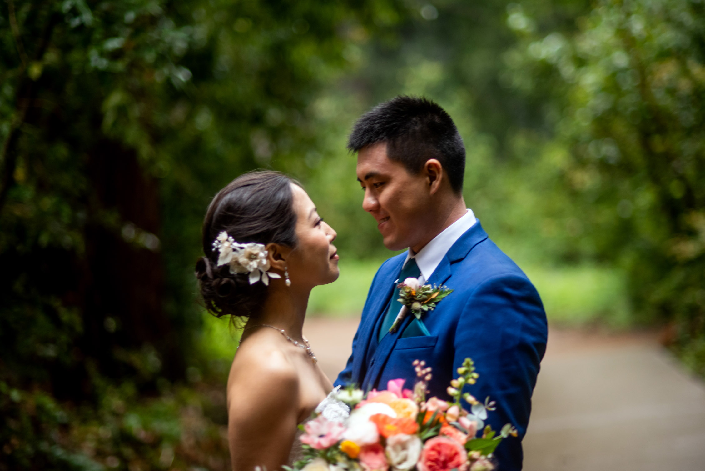 Bride and groom face to face in lush forest with flowers