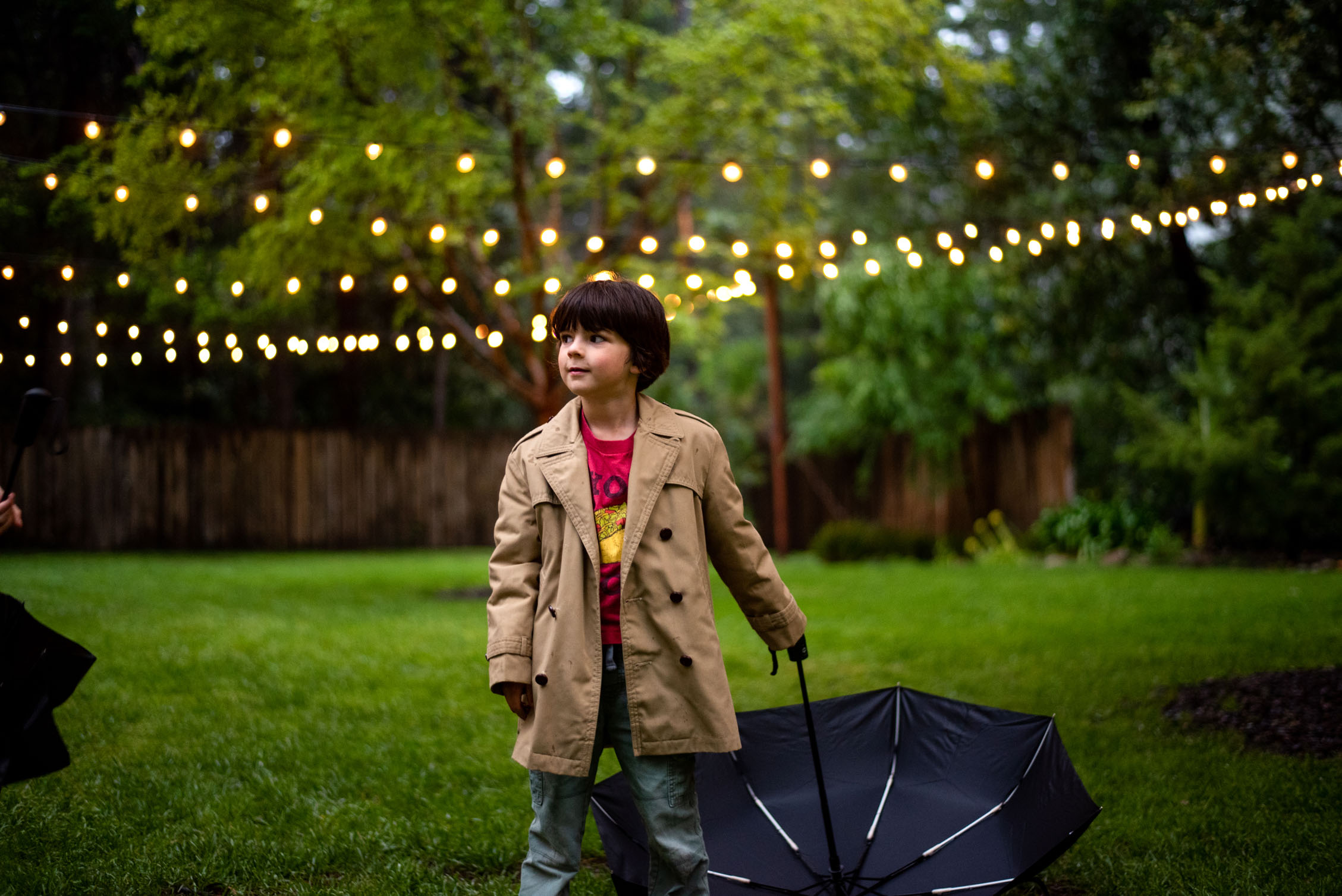 Young boy with umbrella standing under the string lights